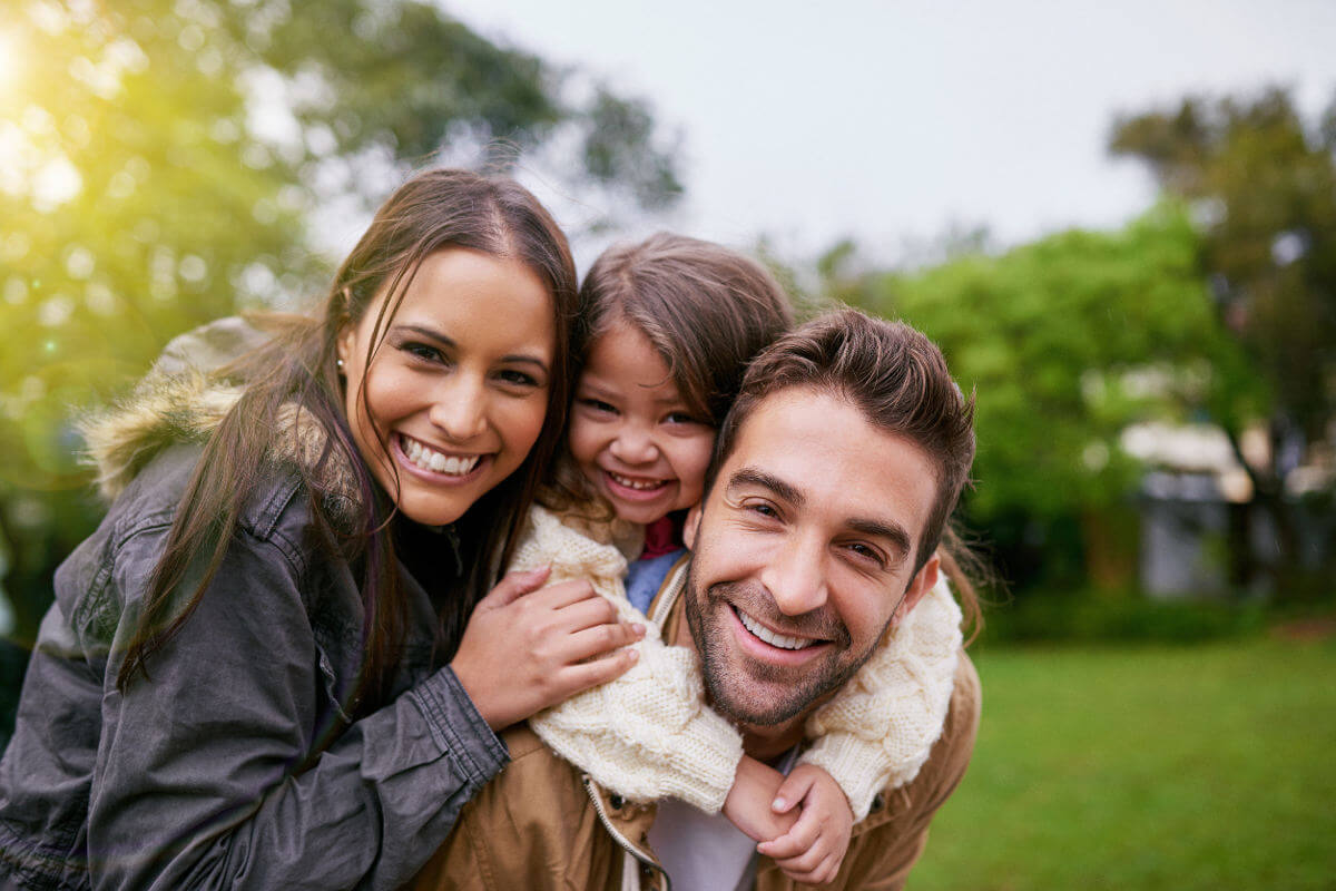 Smiling family of three at park with trees in background